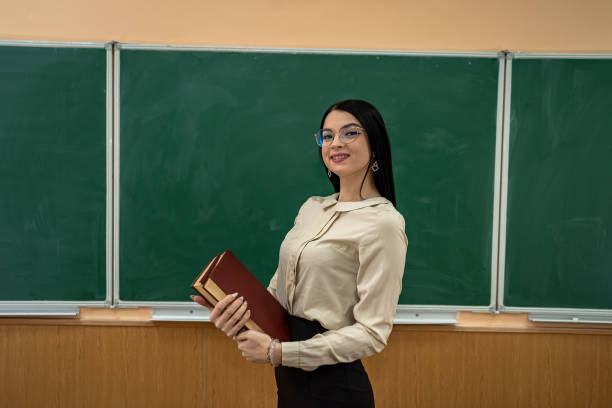 young beautiful elementary school teacher stands on a background of school board. young beautiful elementary school teacher stands on a background of school board. School teacher concept How do I address someone with multiple doctoral stock pictures, royalty-free photos & images