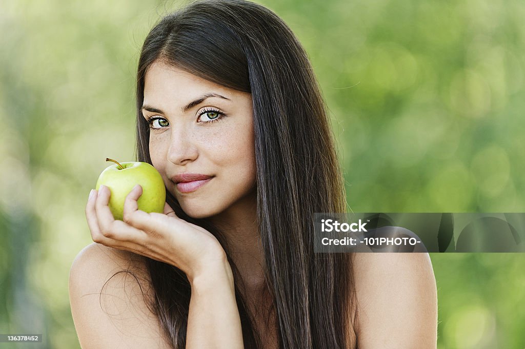 bare woman with an apple in his hand long-haired young woman with bare shoulders holding green apple background summer green park Adult Stock Photo