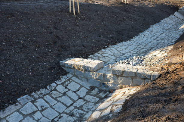 istock Sewer gutter paved with granite stone and dikes drains rainwater by ditch at the highway into the retention reservoir where the water slows down to the sewer through a pipe with a drain grid 1363784841