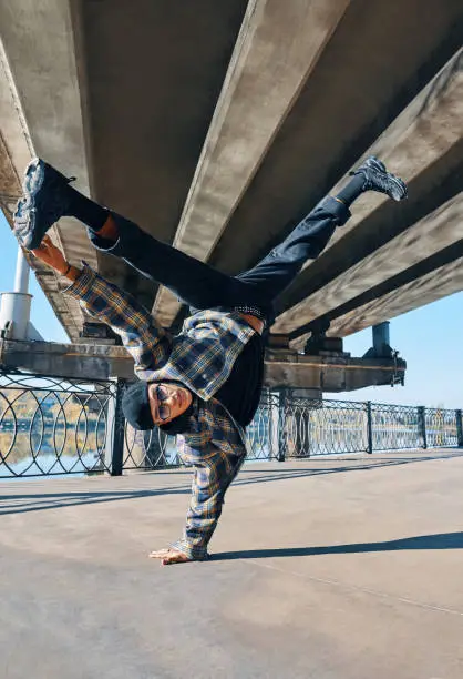 Young man break dancer dancing on urban background performing acrobatic stunts. Street artist breakdancing outdoors