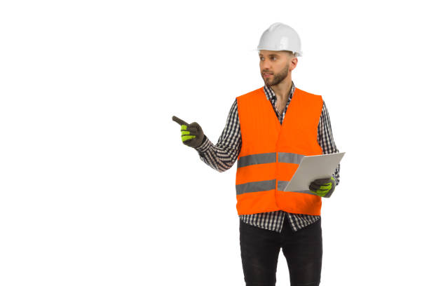 istock Engineer in orange reflective waistcoat and white helmet is standing with documents and pointing to the side. 1363792360