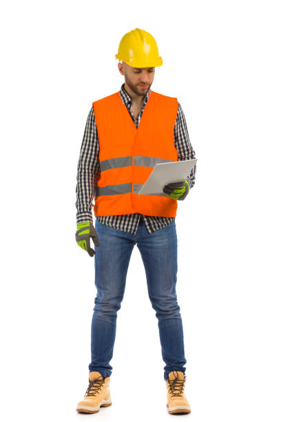 istock Worker in orange reflective waistcoat and white helmet is standing with documents and looking at it. 1363792362