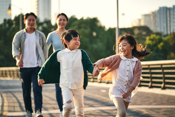 famille asiatique avec deux enfants se promenant dans le parc de la ville - vie citadine photos et images de collection