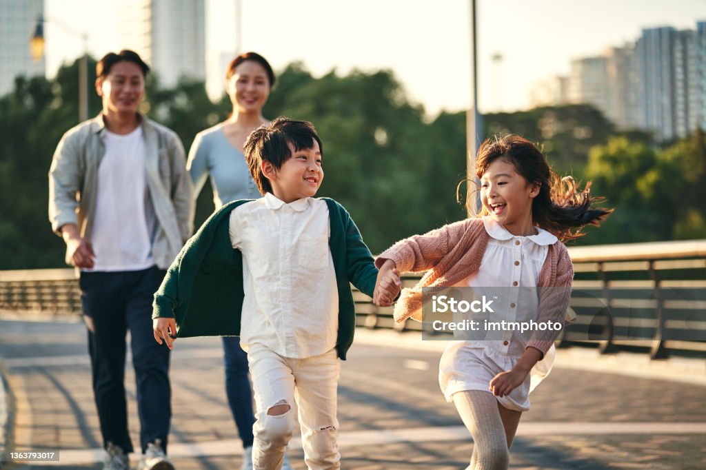 asian family with two children taking a walk in city park happy asian family with two children walking on pedestrian bridge in city park Family Stock Photo