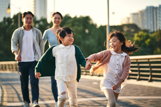 asian family with two children taking a walk in city park happy asian family with two children walking on pedestrian bridge in city park chinese ethnicity stock pictures, royalty-free photos & images