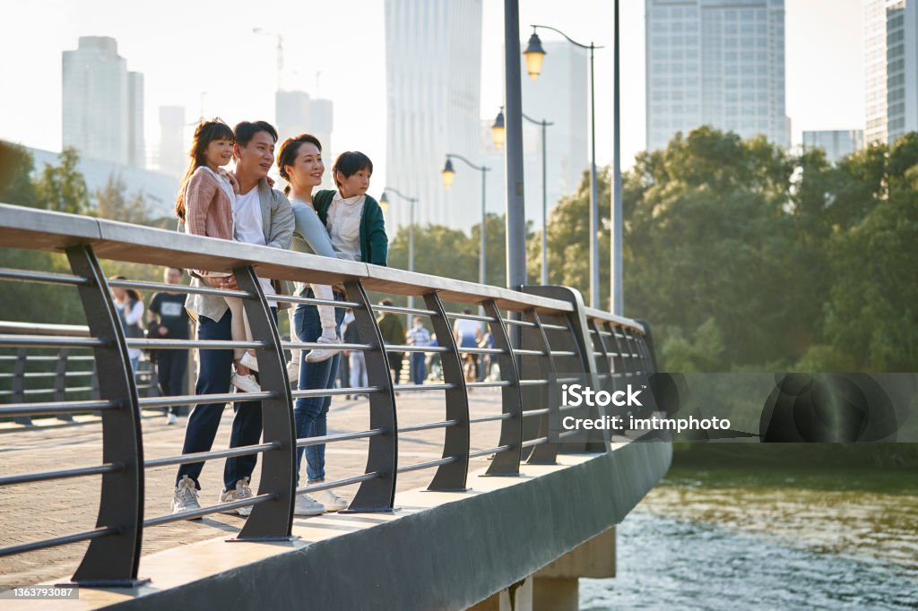 asian family with two children looking at view in city park asian family with two children standing on pedestrian bridge looking at view in city park Footbridge Stock Photo