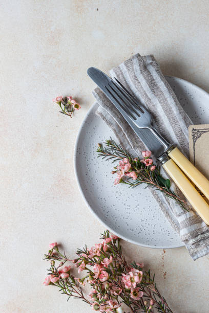 istock Romantic or spring table setting. Knife and fork, little pink flowers and linen napkin on a plate, light concrete background. Flat lay. 1363793329
