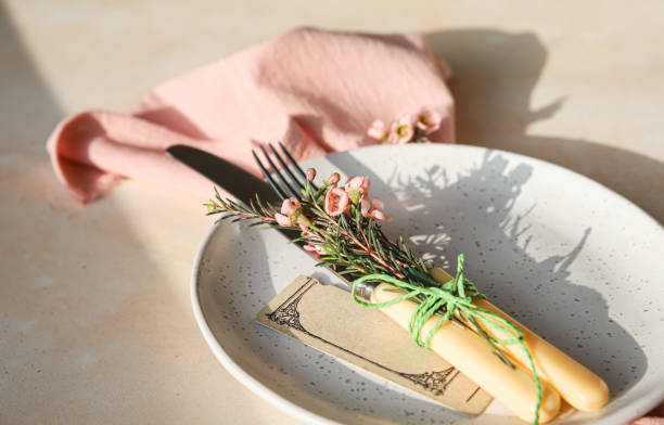 Easter table setting background with plate, cutlery set and pink flowers. Empty plate, advertising, menu. Bright sunlight and hard shadows photography trend.
