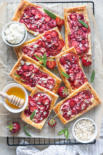 Delicious sweet sliced pies with strawberry. Puff pastry mini pies with strawberry, cream cheese, almond and honey. Top view. Light concrete background.