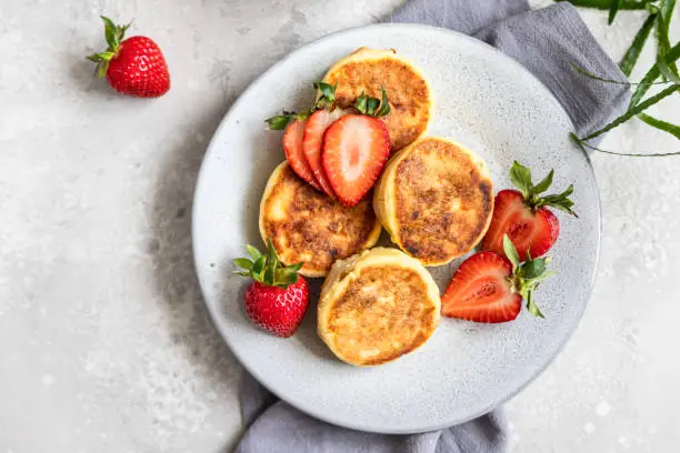 Cottage cheese pancakes or fritters with strawberry and natural yogurt on light background. Healthy breakfast or lunch. Syrniki. Top view.