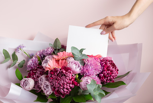 Womens hand holding blank paper card over beautiful bouquet of colorful flowers. Love, Birthday, Valentines day concept