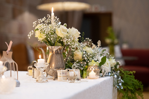 Wedding presidium in restaurant, copy space. Banquet table for newlyweds with flowers, greenery, candles and pink cloth. Lush floral arrangement. Luxury wedding decorations