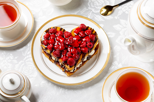 Heart shaped cake with cream and raspberries served with hot tea on white table. Millefeuille or mille feuille, lovely french dessert for Valentine's day.