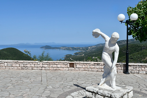 Perdika, Greece - June 29, 2021: Sculpture of a discus thrower on main square in the mountain village in Epirus with Ioanian sea in background