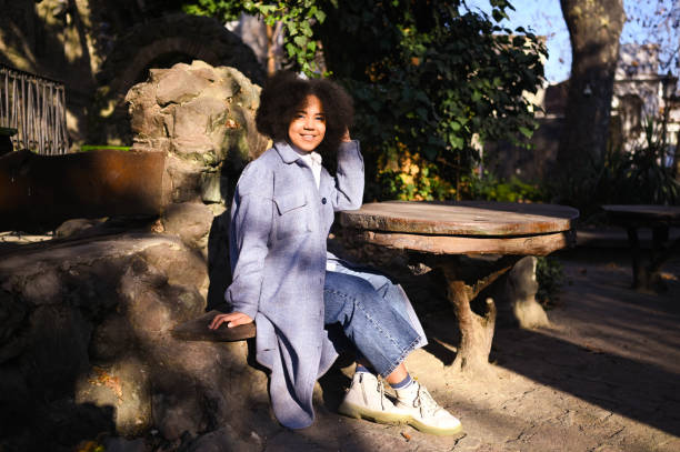 Fashion street style portrait of attractive young natural beauty African American woman with afro hair in blue coat posing outdoors. Happy tourist laughing walks through ancient sights fool around. stock photo