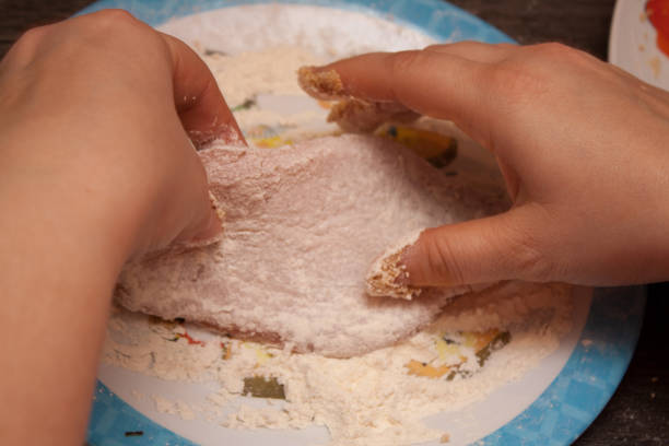 Two hands putting flour on meat to make a wiener schnitzel