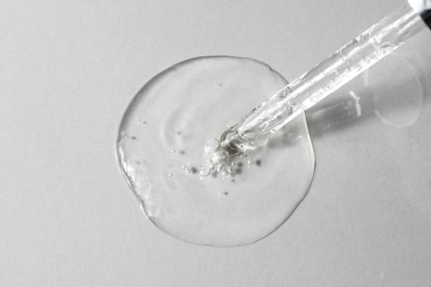 istock Facial serum with bubbles pouring from glass pipette on grey background. Transparent liquid gel with hyaluronic acid closeup. Anti aging cosmetic product for skin care. Top view, flat lay 1363806736