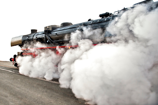 A steam locomotive spits smoke and steam at full speed