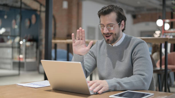 istock Waving Young Man Doing Video Chat in Office 1363817093