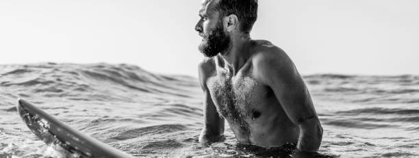 banner horizontal o cabecera con surfista hipster sentado en su tabla de surf en el agua del océano y esperando una gran ola - fit bearded man training with surfboard to sea - hipster people surfing the net internet fotografías e imágenes de stock