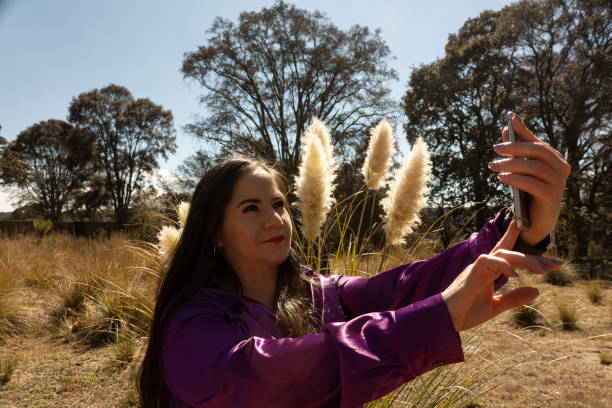 istock Mexican woman taking selfie with her mobile phone in Mexico using technology surrounded by fox tail and grass Polypogon monspeliensis 1363826581