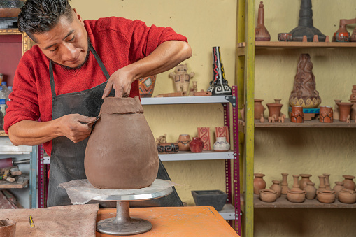 Potter making and shaping a pottery vessel with a tool in his workshop.