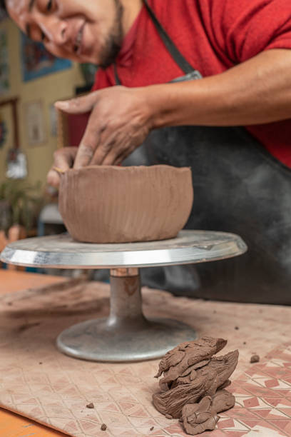 istock Potter molding a clay bowl with a stick in his workshop 1363831151