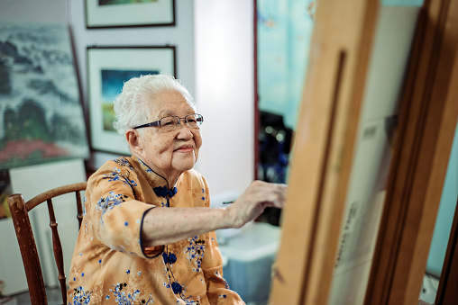 waist up of active mature senior women painting on canvas with easel