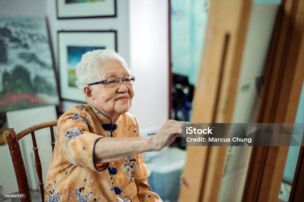 Asian chinese smiling senior women painting on canvas at her house waist up of active mature senior women painting on canvas with easel Senior Adult Stock Photo