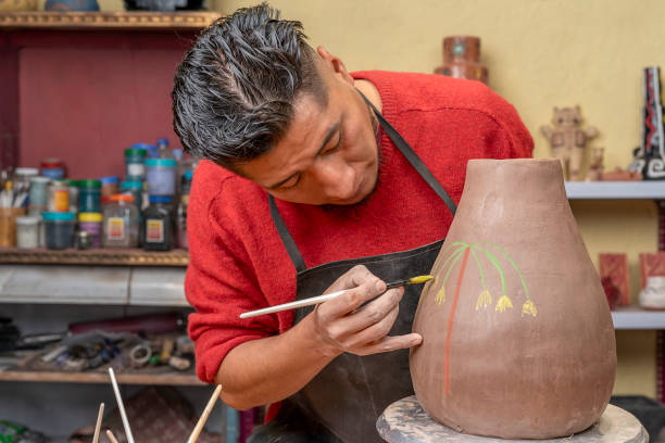 potter using a paintbrush to decorate with drawings a clay pot he has just created in his studio Front view potter using a paintbrush to decorate with drawings a clay pot he has just created in his studio. artist sculptor stock pictures, royalty-free photos & images