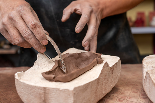 Hands of a potter using a small saw to cut off excess clay from inside a mold