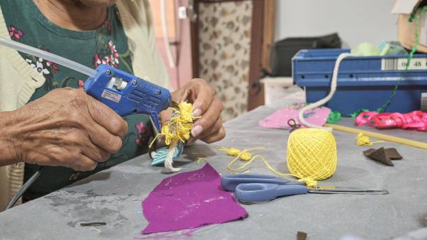 Portrait of an artisan woman at home in her atelier, handcrafting a cloth doll with sustainable materials and cloth remains. Around her there are some tools such as a pen, scissors and sewing threads, used for manufacturing the cloth doll.