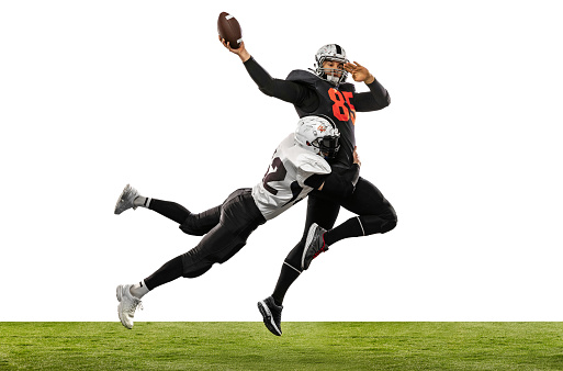 Two american football players in action, motion. Sportsmen fight for ball isolated on white background on grass. Concept of sport, challenges, achievements, active lifestyle. Copy space for ad