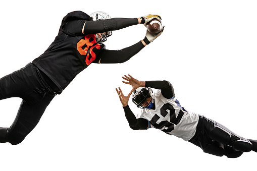 Catch ball in jump. Two american football players in action, motion. Sportsmen fight for ball isolated on white background on grass. Concept of sport, challenges, achievements, active lifestyle.