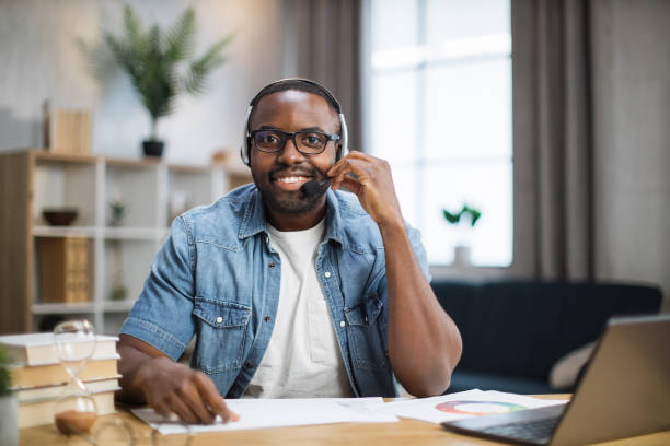 istock Man in headset smiling on camera while sitting at desk 1363833424