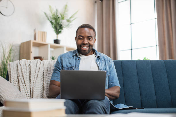 istock Happy african man sitting on couch and using laptop 1363834614