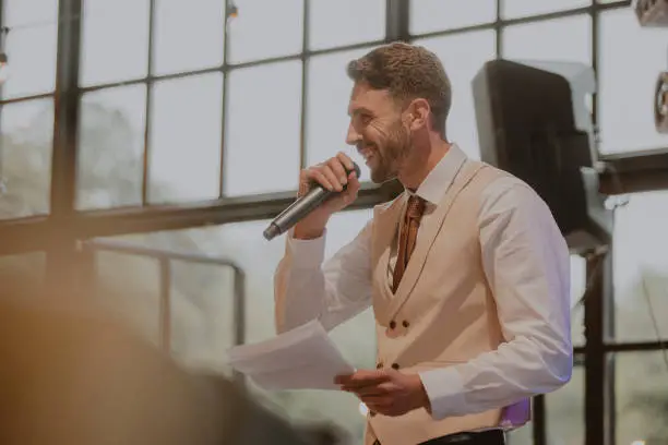 Man making a speech for his sister at an LGBTQI+ wedding in the North East of England. He is wearing a suit, holding a microphone.