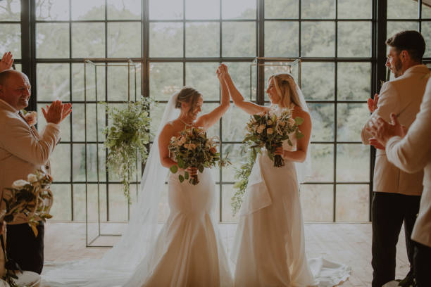 Bride and Bride Two women celebrating at their LGBTQI+ wedding in the North East of England. They are both holding flowers and holding their hands up after saying their wedding vows. civil partnership stock pictures, royalty-free photos & images