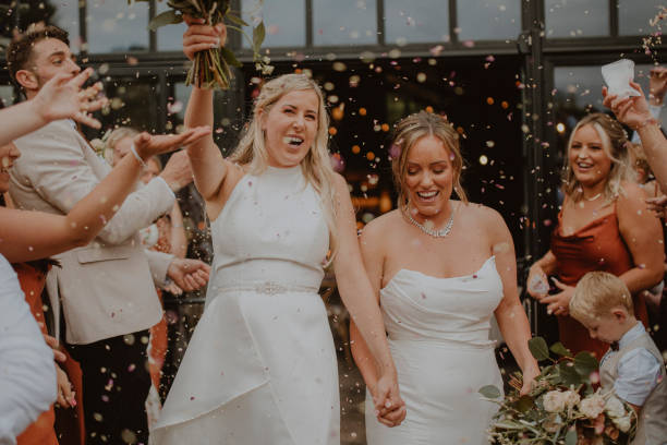 Throwing Confetti at the Brides Two women celebrating at their LGBTQI+ wedding in the North East of England. They are both holding flowers and hands, walking through their guests laughing while everybody throws confetti. civil partnership stock pictures, royalty-free photos & images