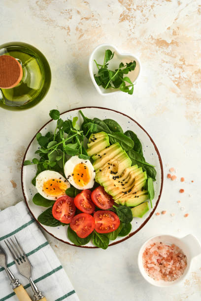 istock Avocado, cherry tomato, spinach and chicken egg, microgreens peas and black sesame seeds fresh salad in bowl on white stone table background. Healthy breakfast food concept. Top view. 1363836335