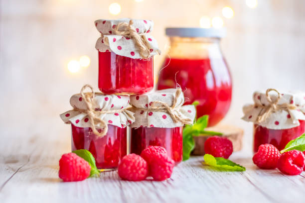 himbeermarmelade in kleinen gläsern wird auf den holzschreibtisch gelegt. hausgemachte marmelade aus frischen himbeeren. frische und gesunde küche. - jar canning food preserves stock-fotos und bilder