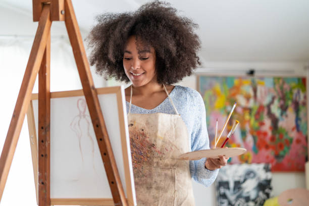 istock Afro female fine artist  drawing in studio on a canvas, placed on a tripod 1363837237