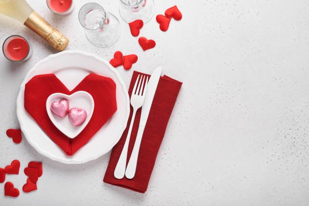 istock Valentinas day table setting white color with white silverware, red napkin folded as heart, candles, champagne, glasses on white background for greetings. Romantic dinner or menu concept. Mock up. 1363837786