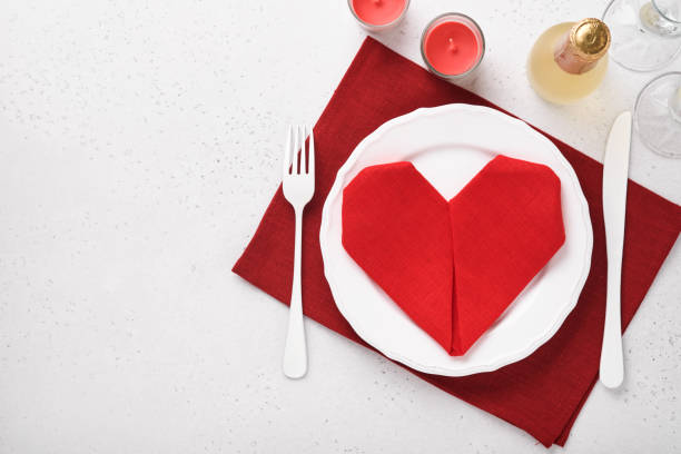 istock Valentinas day table setting white color with white silverware, red napkin folded as heart, candles, champagne, glasses on white background for greetings. Romantic dinner or menu concept. Mock up. 1363837808
