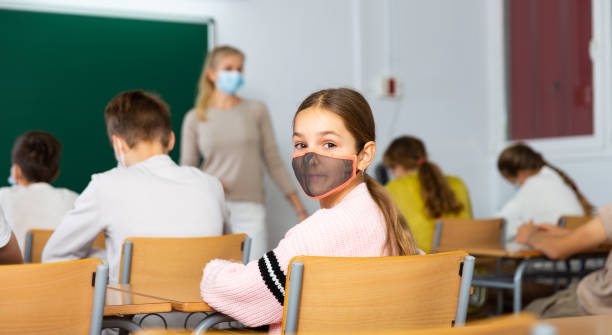 istock Student in protective mask studying in classroom, listening to lecturer and writing in notebook 1363838931