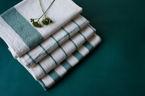 Istanbul, Turkey-January 6, 2022: Folded and stacked linen dish towels on a teal green background. Dish towels are clean washed and have green stripes and lines on white. Dish towels have green wildflower on it. Shot with Canon EOS R5.