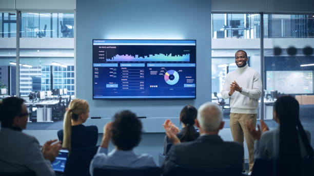istock Presentation Event: On-Stage Black Businessman Speaker Presents Startup Big Data Statistics, Charts, Revenue Growth Infographics. Conference for Group of Diverse Investors, Businesspeople Applaud 1363841562