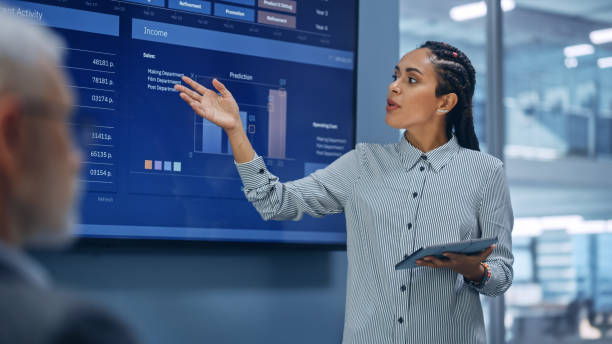 istock Diverse Modern Office: Successful Black Digital Entrepreneur Uses Tablet Computer and TV Screen with Big Data, Statistics, Talks about Company Growth. Investor, Top Managers, Executives Discuss Graphs 1363841722
