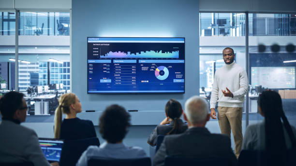 istock Modern Product Presentation Event: On-Stage Successful Black Businessman Speaker Presents e-Commerce Startup Big Data Statistics, Charts, Revenue Growth Infographics. Live Event. Press Conference 1363841726