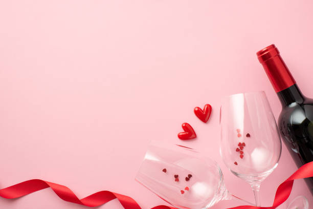 foto vista dall'alto di san valentino decorazioni rosso nastro riccio piccoli cuori tra due bicchieri di vino con coriandoli e bottiglia di vino su isolato sfondo rosa pastello con spazio vuoto - heart shape confetti small red foto e immagini stock